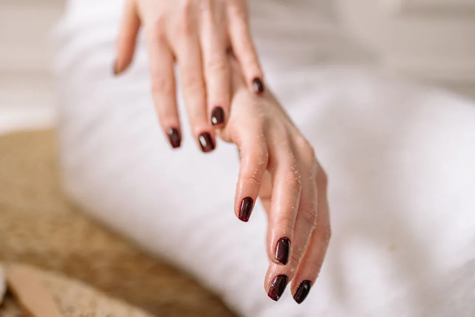 Close-up of a woman's hand with dark polished nails against a spa backdrop.