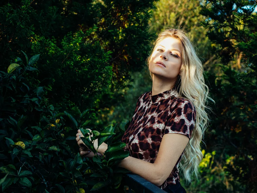 Blonde woman in animal print shirt posing amidst greenery, Curitiba, Brazil.