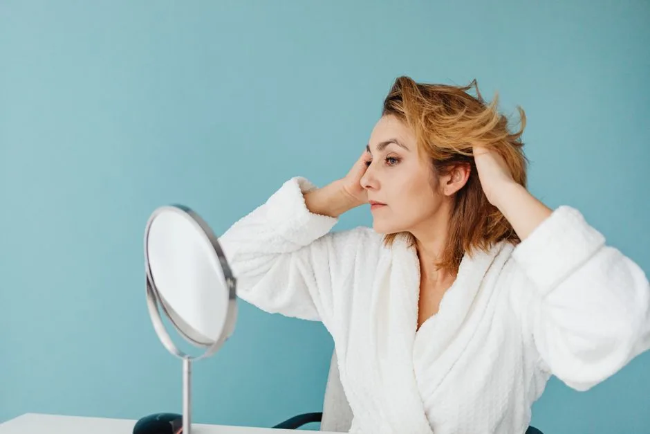 Adult woman in a bathrobe fixing her hair in front of a mirror against a blue background.