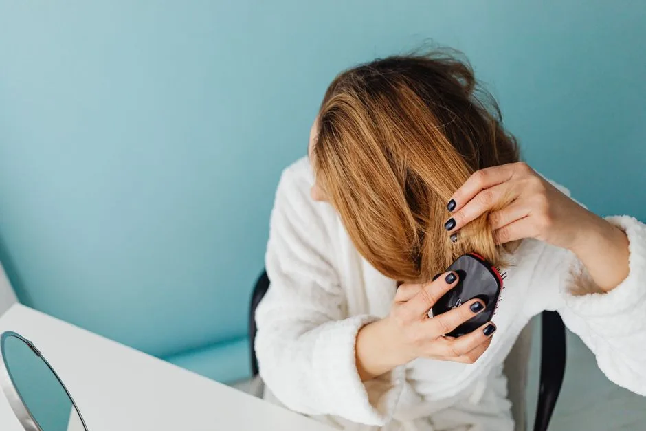 A woman in a bathrobe combs her hair reflecting self-care and relaxation.