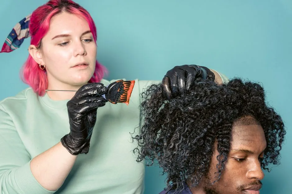 Serious woman with dyed hair applying paint on hair of African American model in studio against blue background