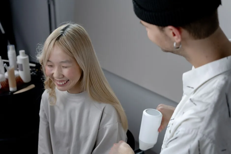 A hairstylist using a blow dryer on a smiling Asian woman in a hair salon.