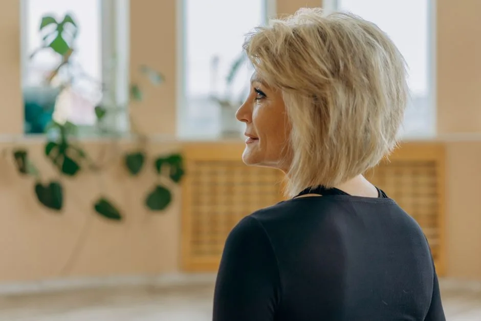 Elegant side profile of a mature woman with blonde hair indoors, facing a window.