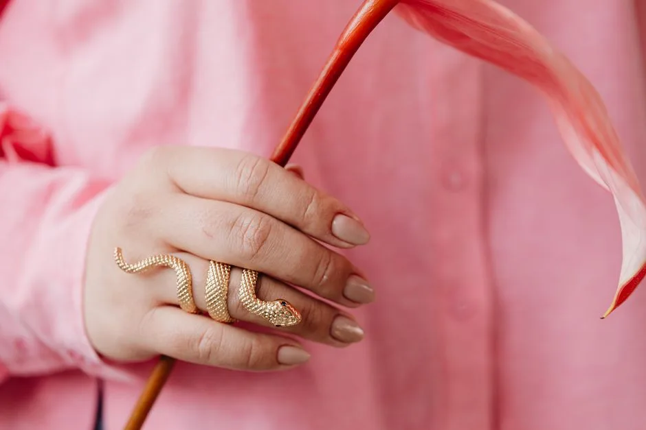 Close-up of a hand with manicured nails holding a flower and wearing a gold snake ring.