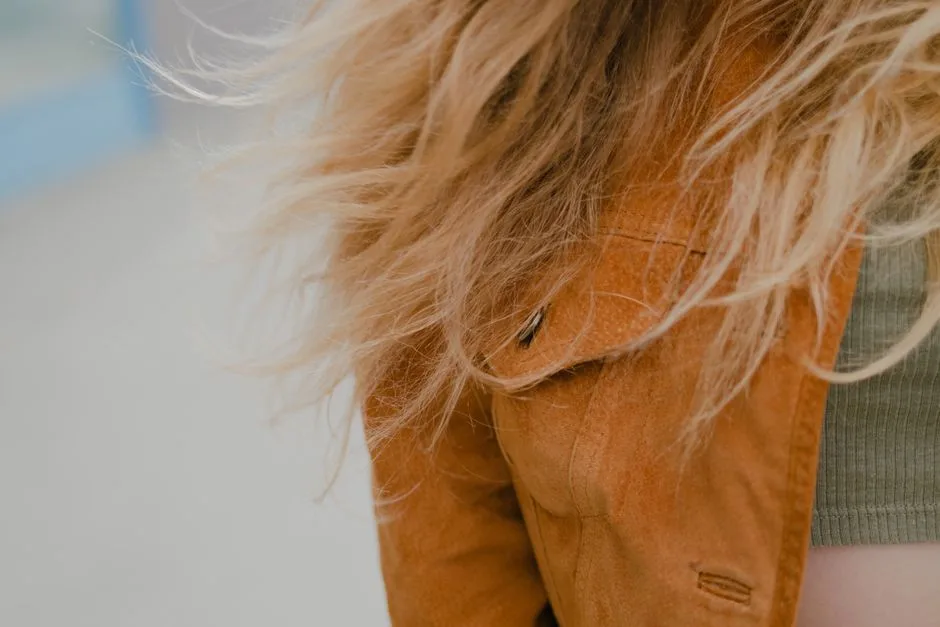 Close-up image focusing on flowing blonde hair and a brown jacket, outdoors.