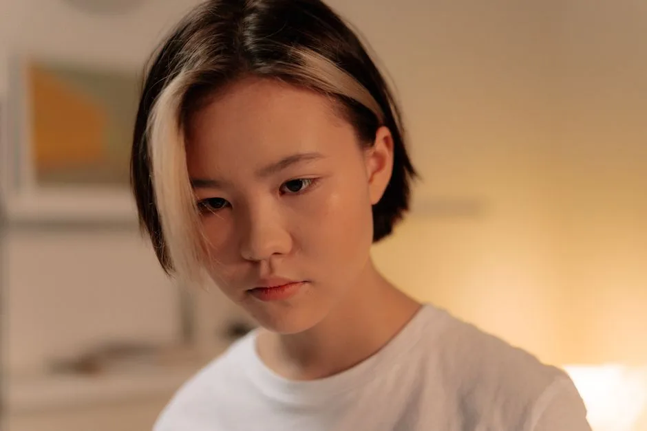 A thoughtful young woman with short, stylish two-tone hair in a soft indoor setting.