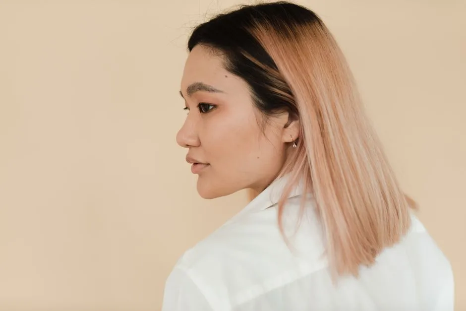 A close-up side profile of a woman with colored hair against a neutral background.