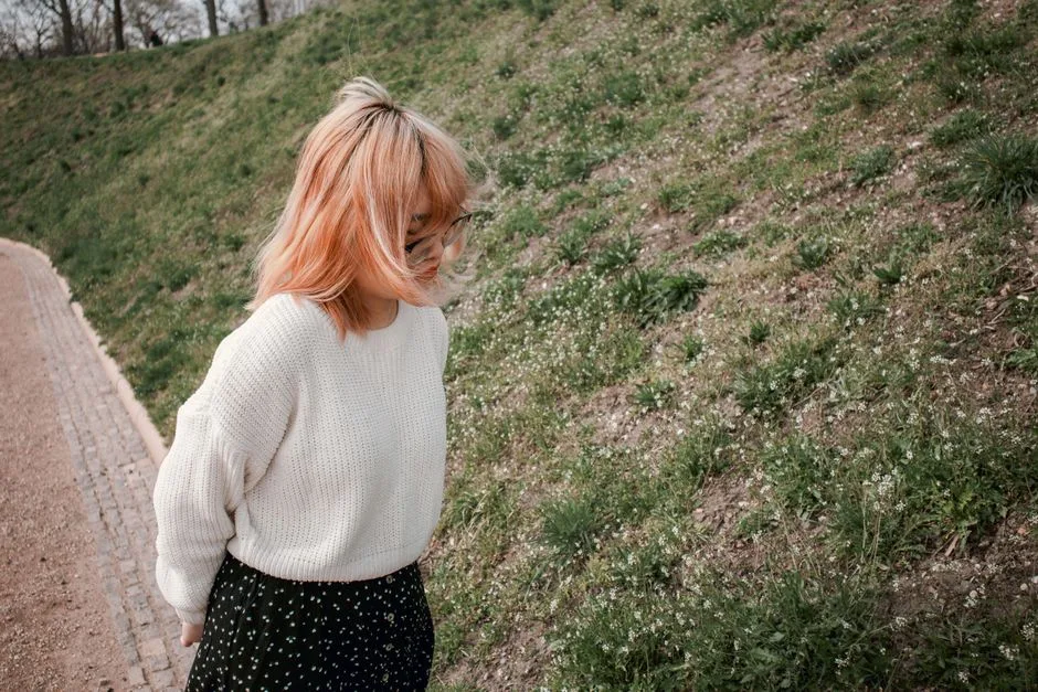 Woman with glasses and blonde hair walking in a spring park wearing a knitted sweater.