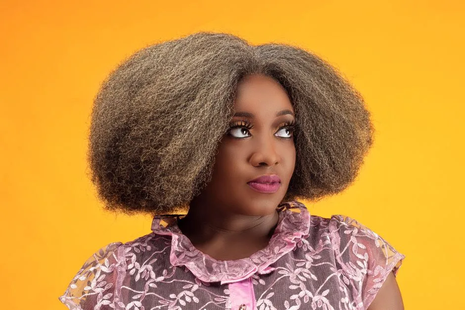 Stylish portrait of a woman with afro hair, wearing a lace blouse against a yellow background.