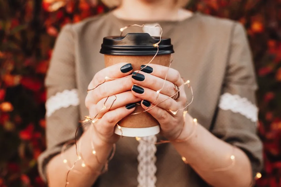 Close-up of hands holding a coffee cup with fairy lights, capturing autumn warmth.