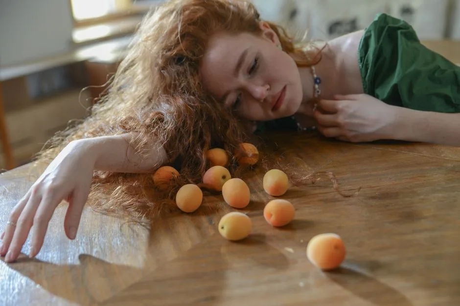 A woman lies pensively with apricots on a wooden table, creating a reflective mood.