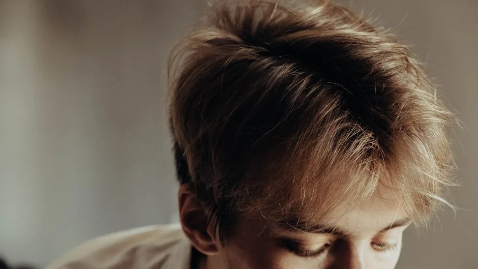 A detailed close-up image showcasing a young man's stylish haircut with tousled, light brown hair.