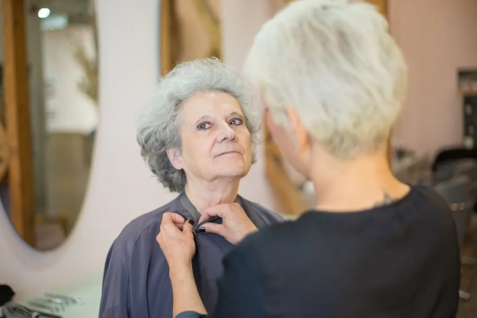 Senior woman getting ready in a hair salon, assisted by a hairstylist adjusting her cape.