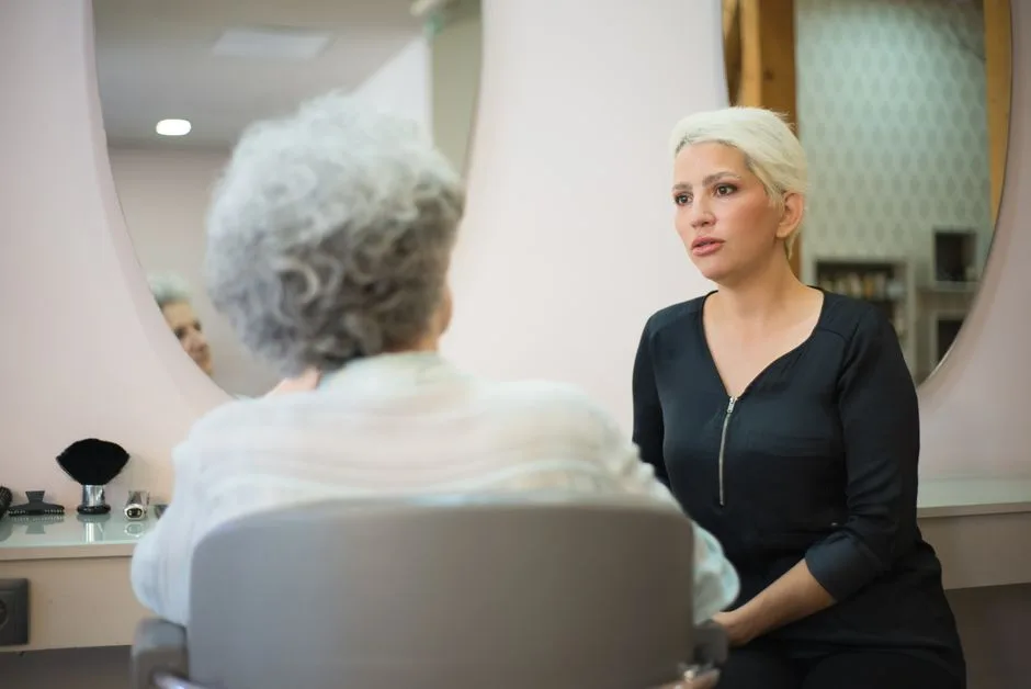 Two women having a conversation in a salon setting with a mirror reflecting their interaction.