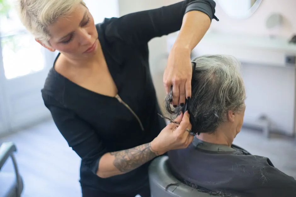 A hair stylist with a tattoo cutting a client's hair in a salon.