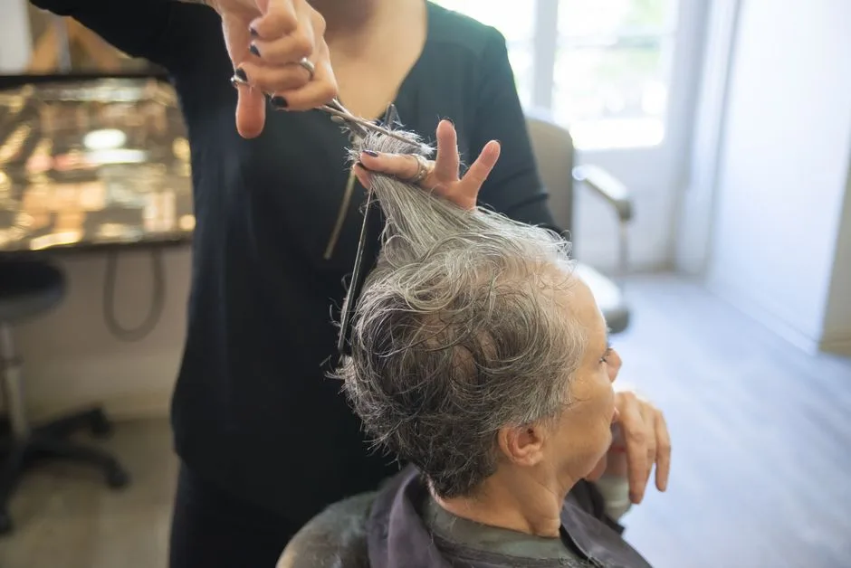 A hairdresser styles a senior woman's hair in an indoor salon setting.