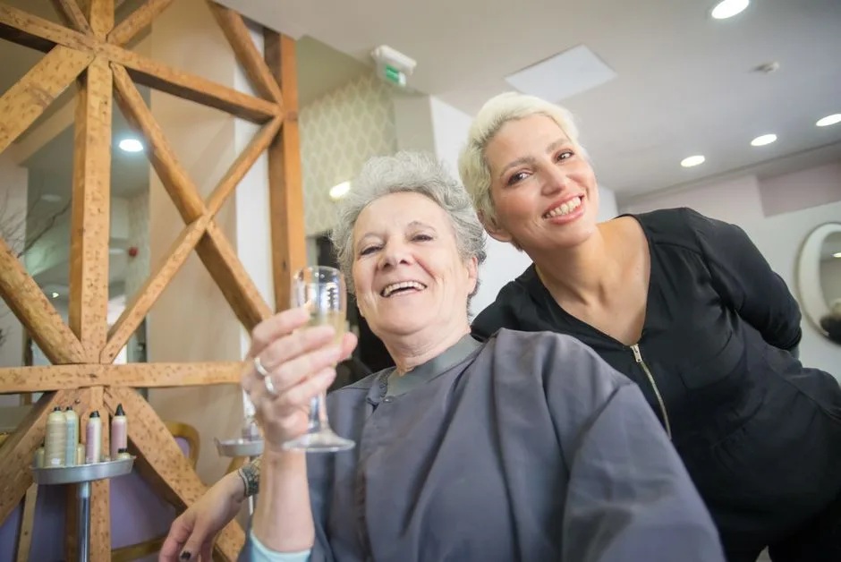 Happy senior woman and hairstylist smiling in a hair salon in Portugal.