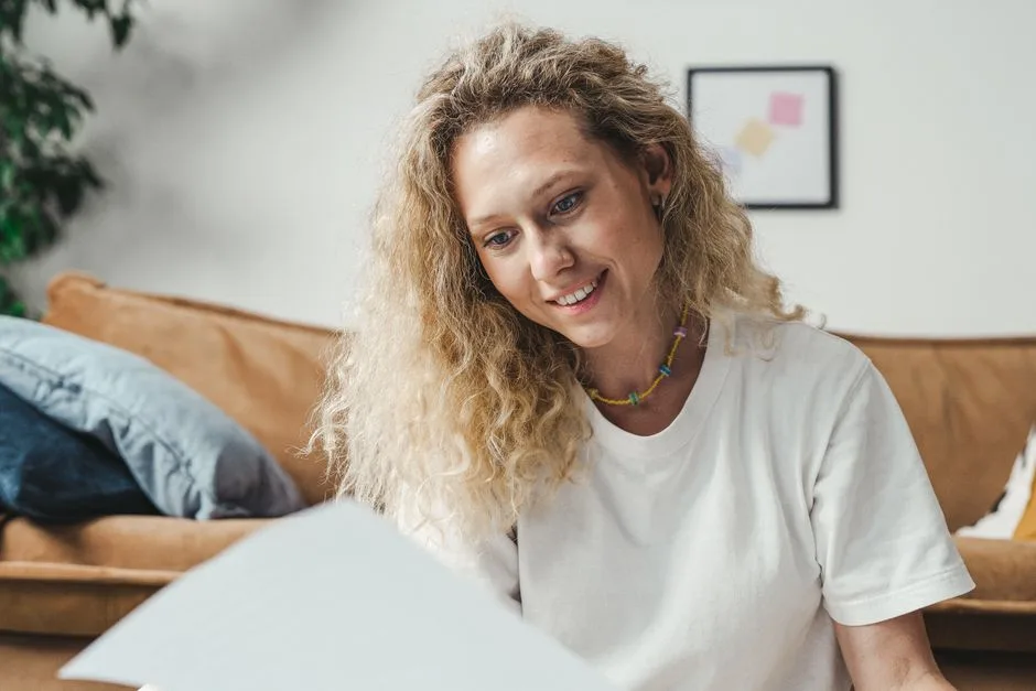 Woman with curly blonde hair smiling while holding papers in a cozy indoor setting.