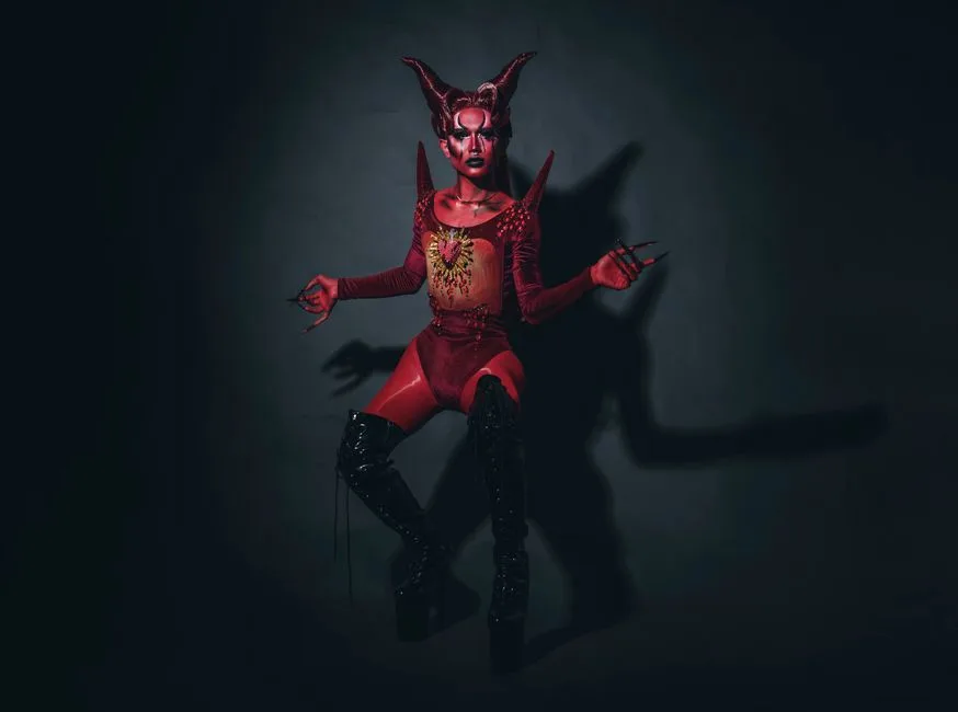 A striking depiction of a woman in a devil costume with body paint and platform boots in a studio setting.