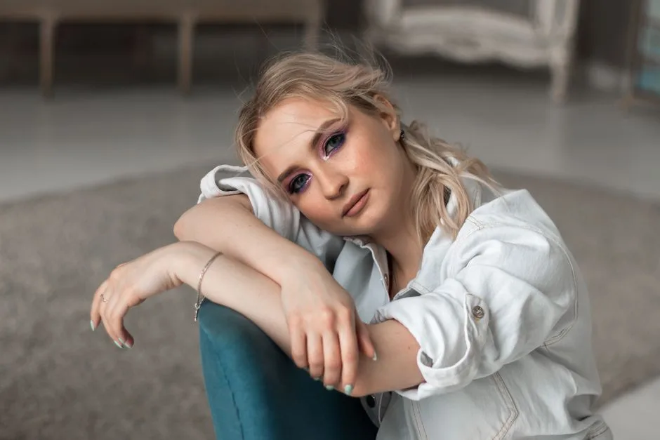 Elegant portrait of a woman with striking makeup and a relaxed pose indoors.