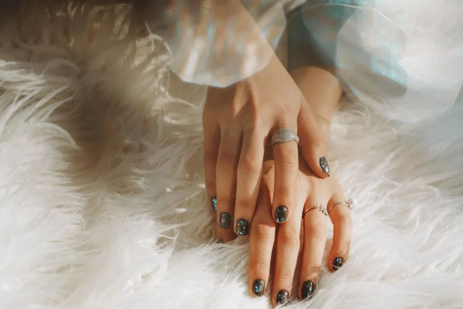 Close-up of a woman's hands wearing rings and nail art, resting on white faux fur.