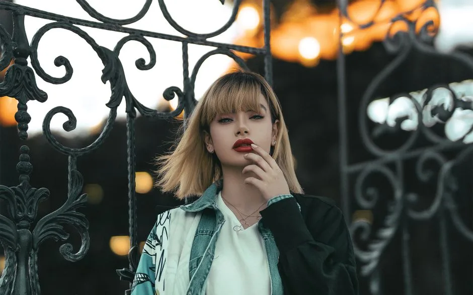 Elegant woman with red lips and blond hair posing in front of an intricate gate.