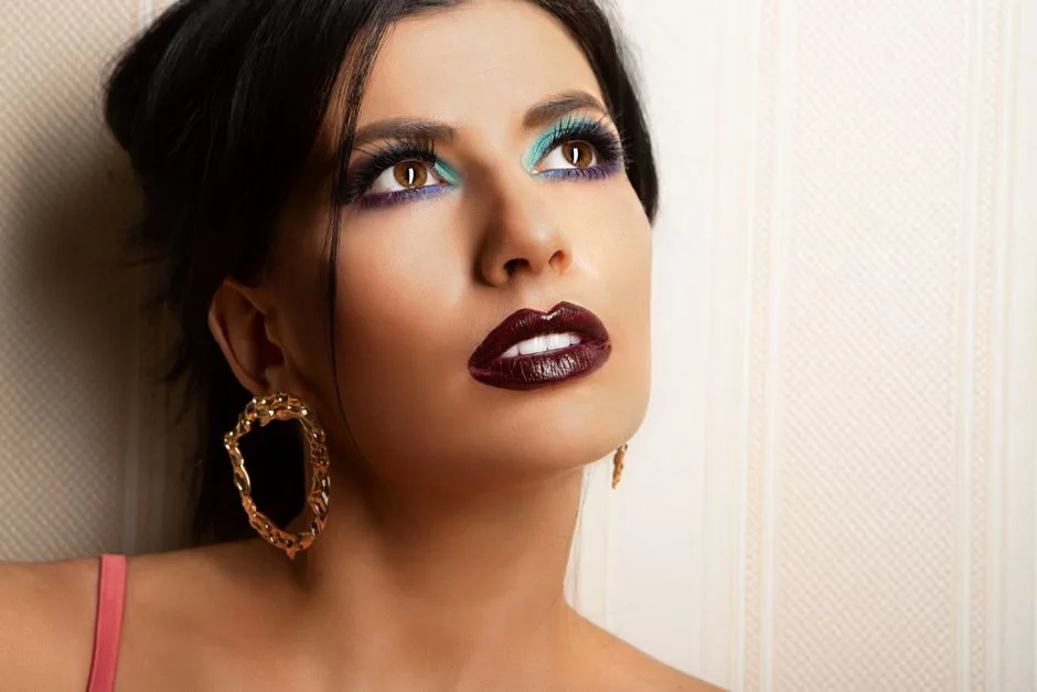 Close-up of a woman with dramatic makeup and earrings looking upwards, exuding glamour.