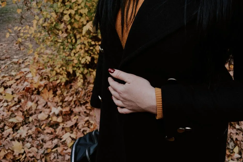 Woman with dark coat and painted nails standing near fall leaves in Kherson, Ukraine.