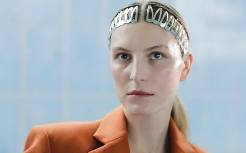 Close-up portrait of a woman wearing a stylish metal hair clip and an orange blazer.