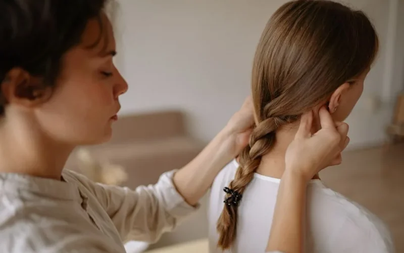 Close-up of a woman braiding another woman's hair indoors, evoking tranquility.