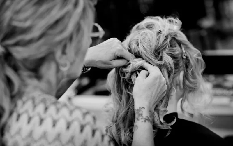 Black and white photo of a hairstylist crafting an elegant updo on a woman's hair.