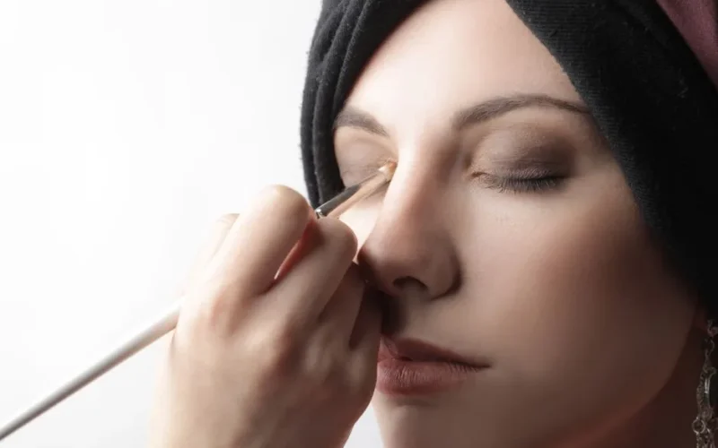 Elegant close-up of a woman applying eye makeup with a brush indoors.