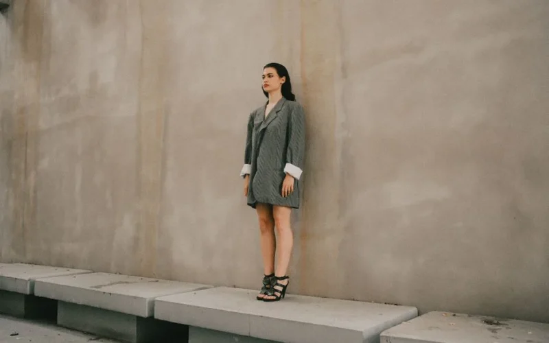 Stylish woman standing against a concrete wall, wearing an oversized blazer.