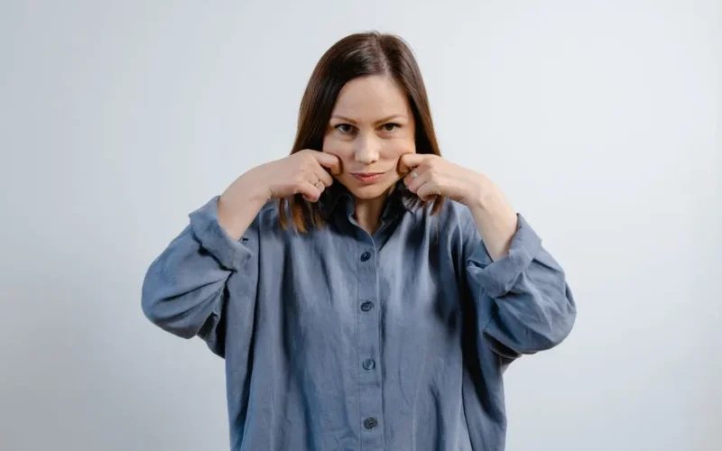 A woman demonstrates facial exercises, promoting wellness and skin care routines.