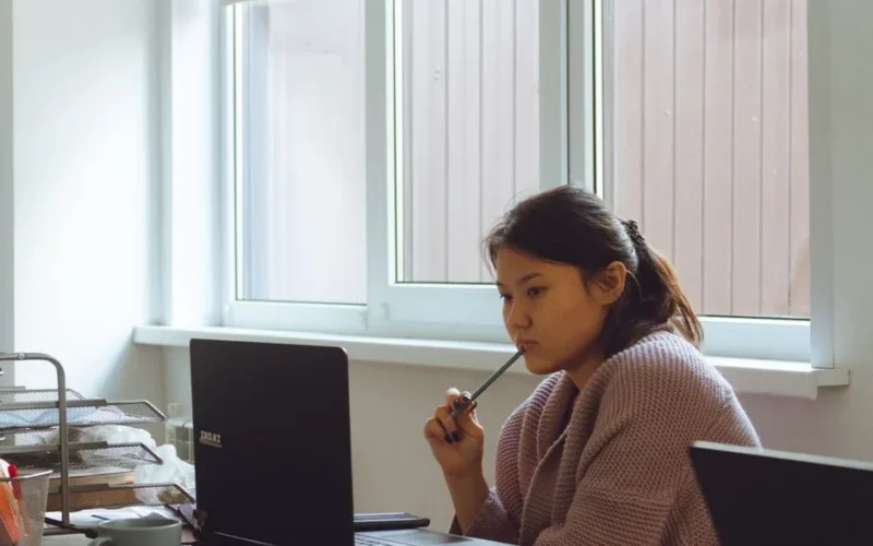 Young woman in cozy sweater working intently on laptop at desk.