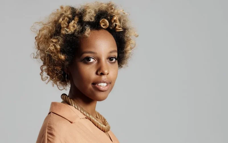Portrait of a stylish young woman with afro hair, wearing a necklace in a studio setting.
