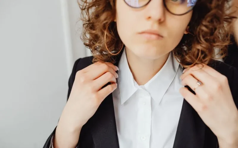 Close-up of a confident woman in a black blazer and white shirt adjusting collar.