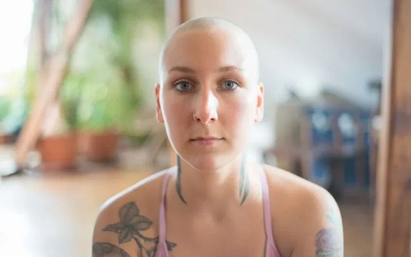 Intimate portrait of a woman with a buzz cut and tattoos in a serene indoor setting.