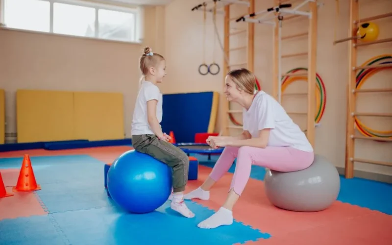 Happy mother and daughter bonding on exercise balls in an indoor gym setting.