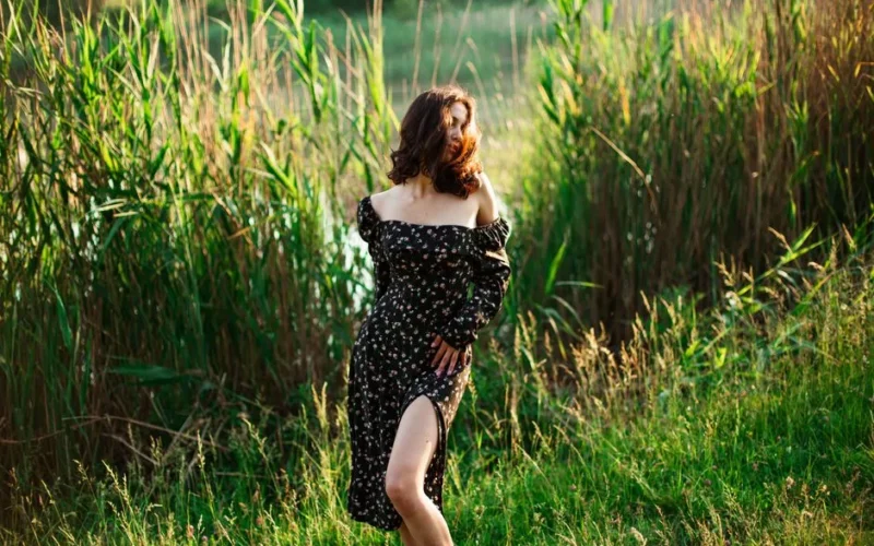 A woman in a floral dress enjoys a sunny summer day surrounded by lush greenery, exuding vintage charm.