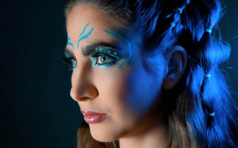 Close-up portrait of a woman with striking blue artistic makeup and braided hair.