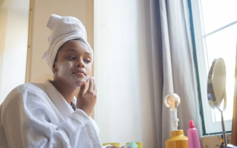 A woman in a bathrobe applying face cream, embodying a calm home spa skincare routine.