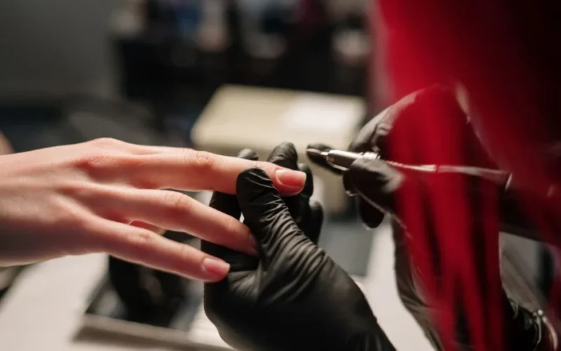 Detail of a manicure in progress with a technician wearing black gloves.