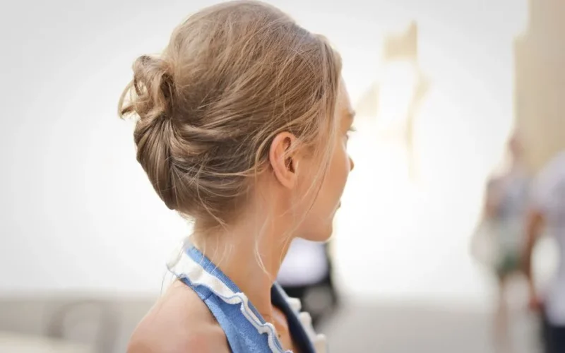 Side view of a woman with blonde hair styled in an updo, against a blurred indoor background.