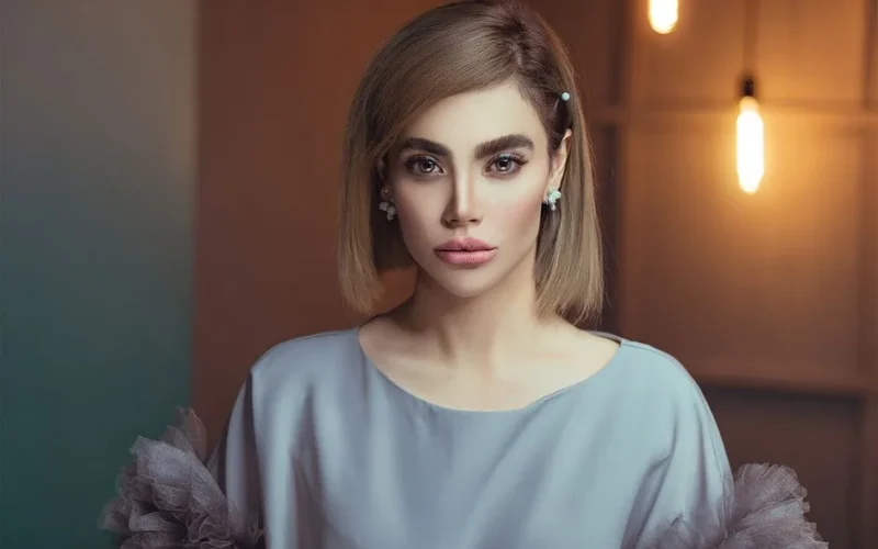 A sophisticated portrait of a woman indoors with modern lighting, featuring elegant attire and makeup.