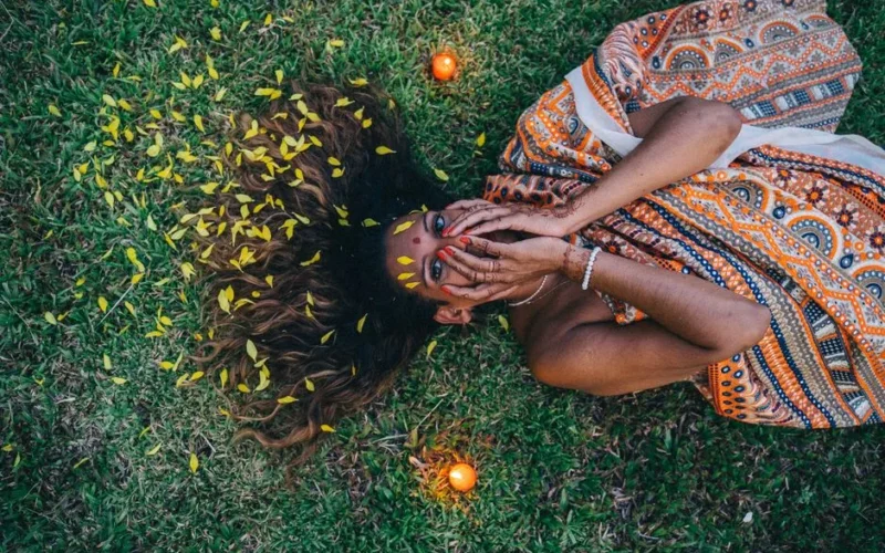 Indian woman lying on grass, adorned with henna and vibrant sari, surrounded by candlelight, creating a serene atmosphere.