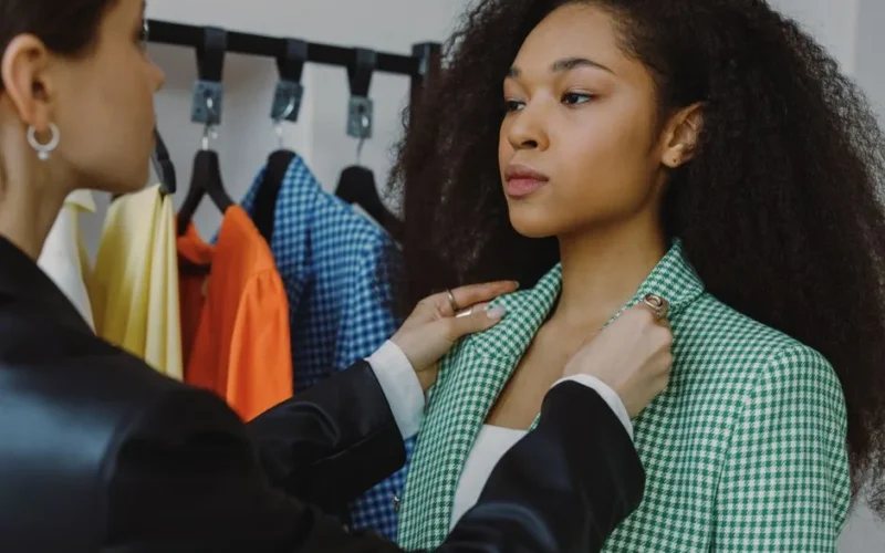 A stylist adjusts a plaid blazer on a model during a fashion consultation, in a boutique setting.