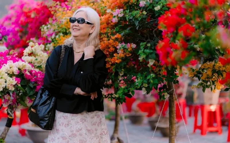Stylish senior woman in sunglasses enjoying colorful bougainvillea garden outdoors.