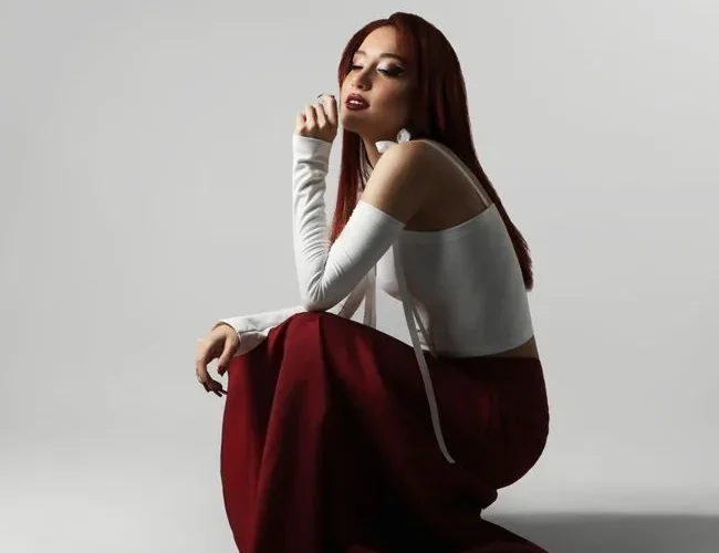 Elegant fashion portrait of a woman in red skirt and white top sitting on studio floor.