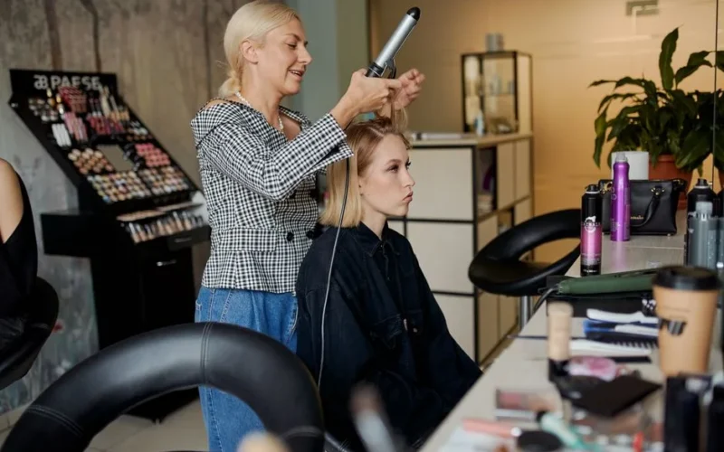 Side view of adult hairstylist straightening hair of client with iron in hairdressing salon